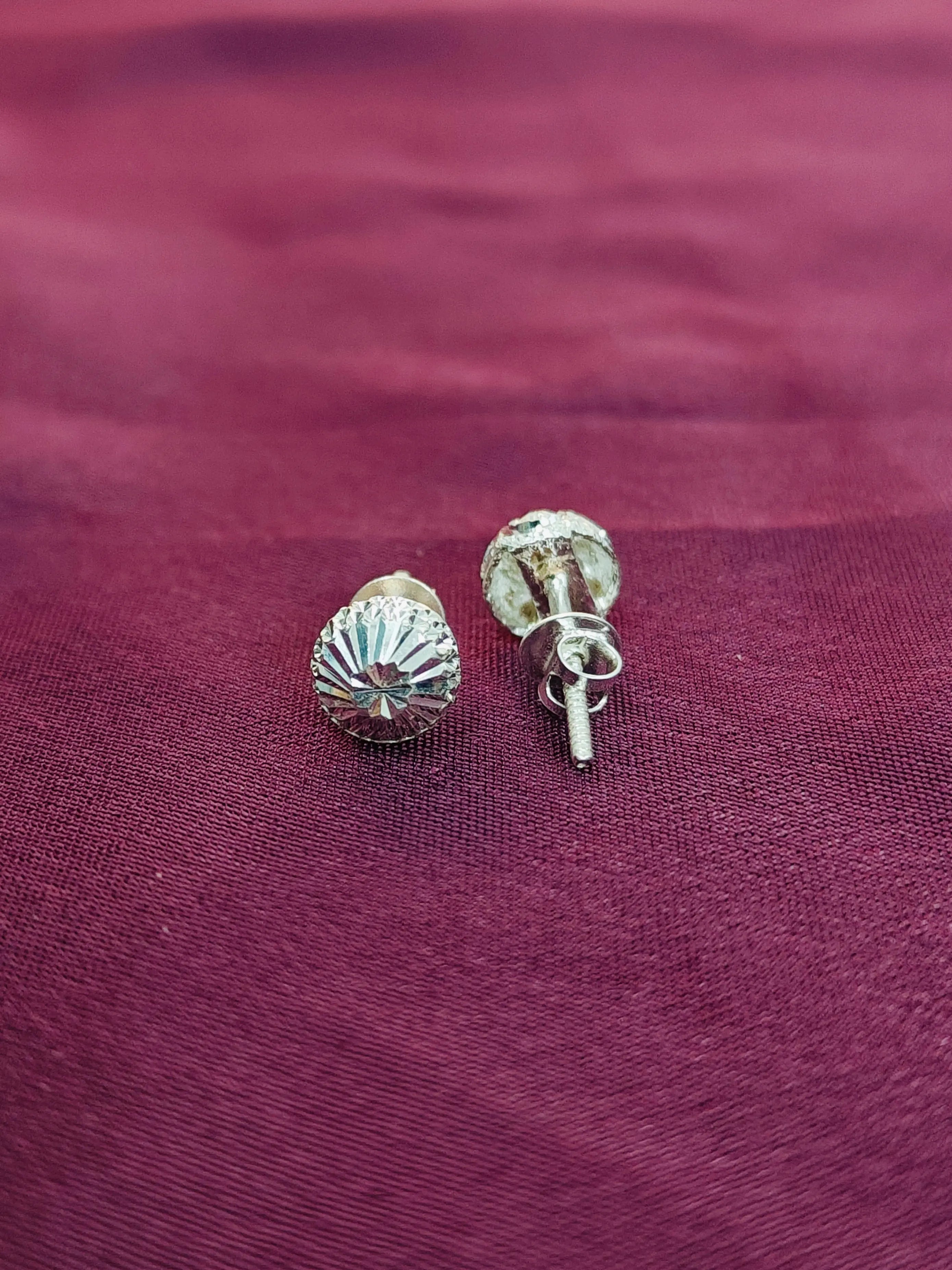 Silver shell-shaped earrings on a maroon fabric background